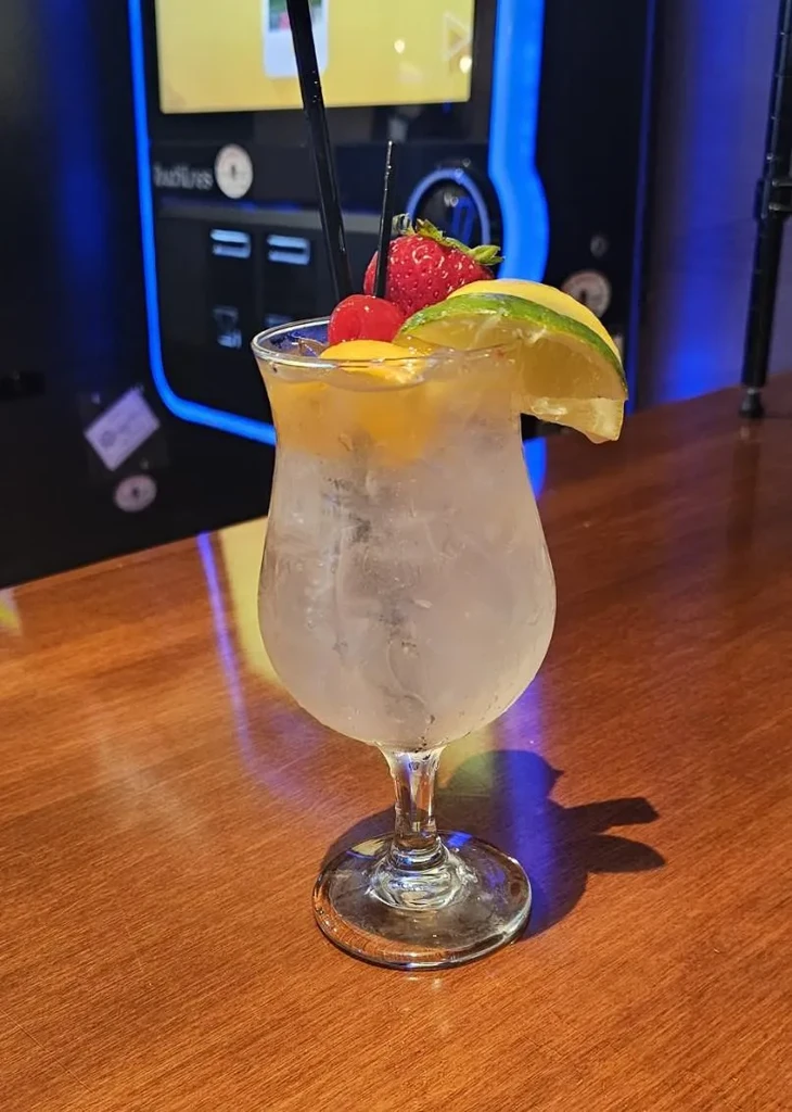 Close-up of a cold fruit-garnished cocktail with straws, background jukebox.