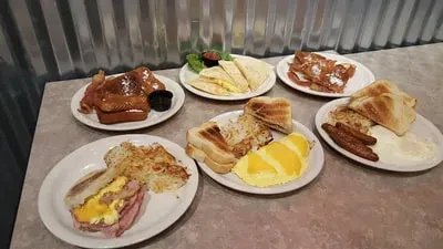 Six distinct breakfast dishes on plates on a grey table.