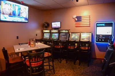 Bar interior featuring electronic gaming machines, tables, chairs, and multiple TVs.