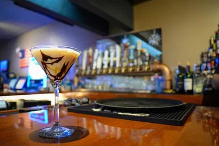 Creamy cocktail in martini glass with dark drizzles on a bar.