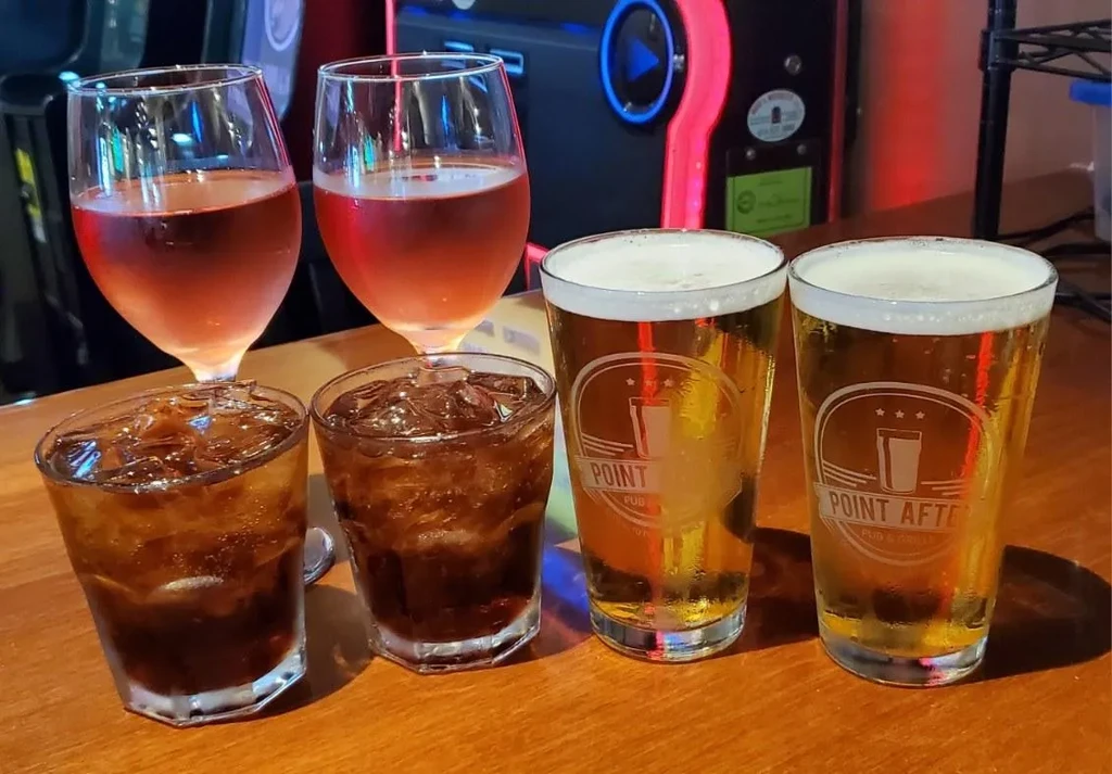 Six drinks: dark soda, rosé wine, and branded beer on a bar.