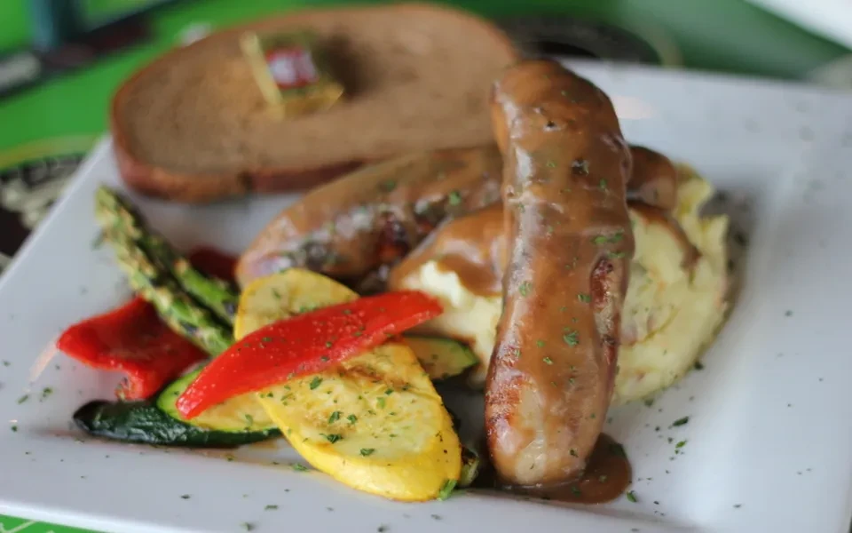 Close-up of sausages with gravy, mashed potatoes, and roasted vegetables.
