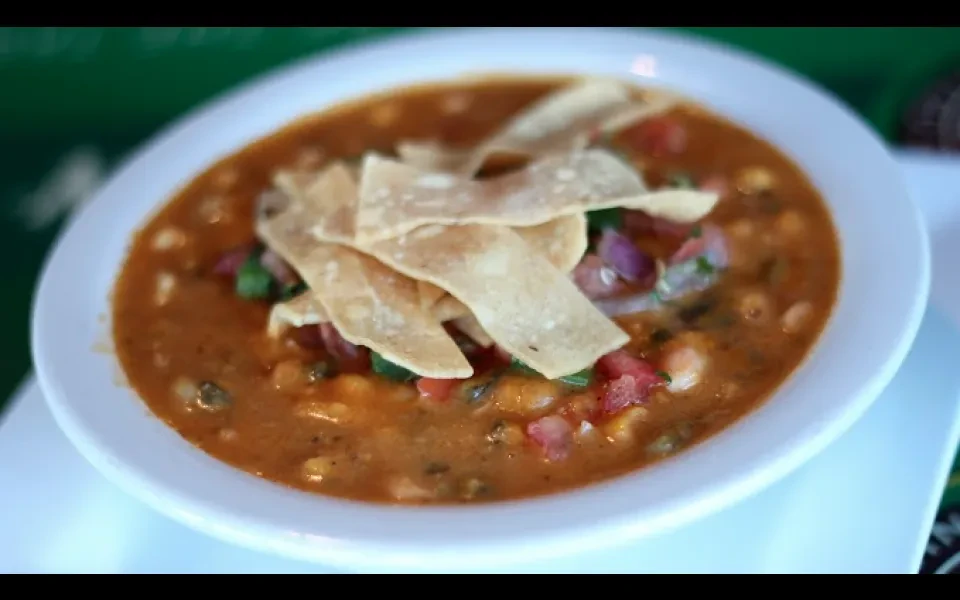 Top-down: Soup with tortilla strips, corn, tomatoes, onions, and cilantro.
