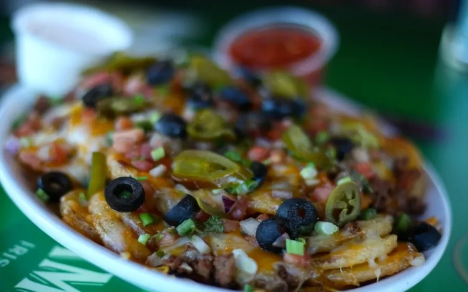 Loaded nachos or fries with melted cheese, meat, and vegetables.