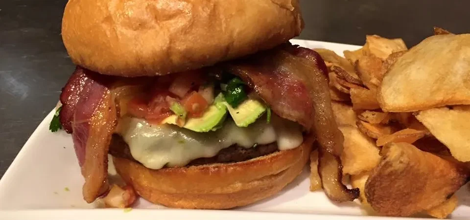 Gourmet burger with avocado, pico de gallo, bacon, and potato chips.