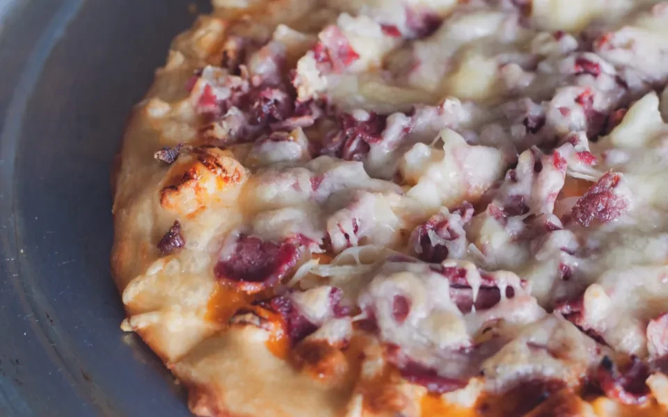 Close-up overhead of freshly baked pizza with cheese and red meat toppings.