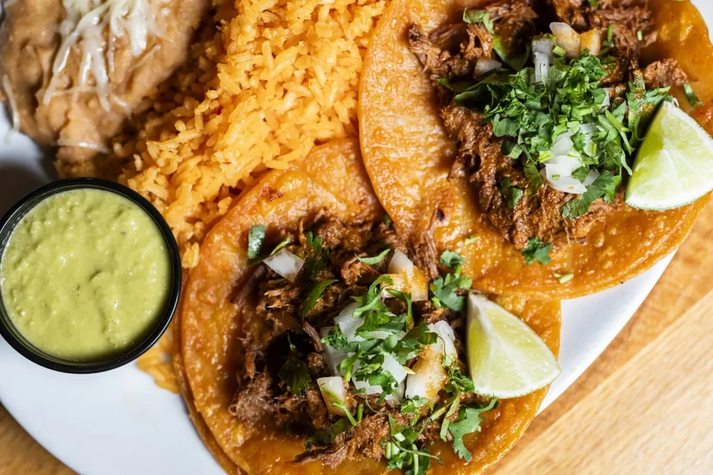 Plate of two fried tacos, Mexican rice, refried beans, and guacamole.
