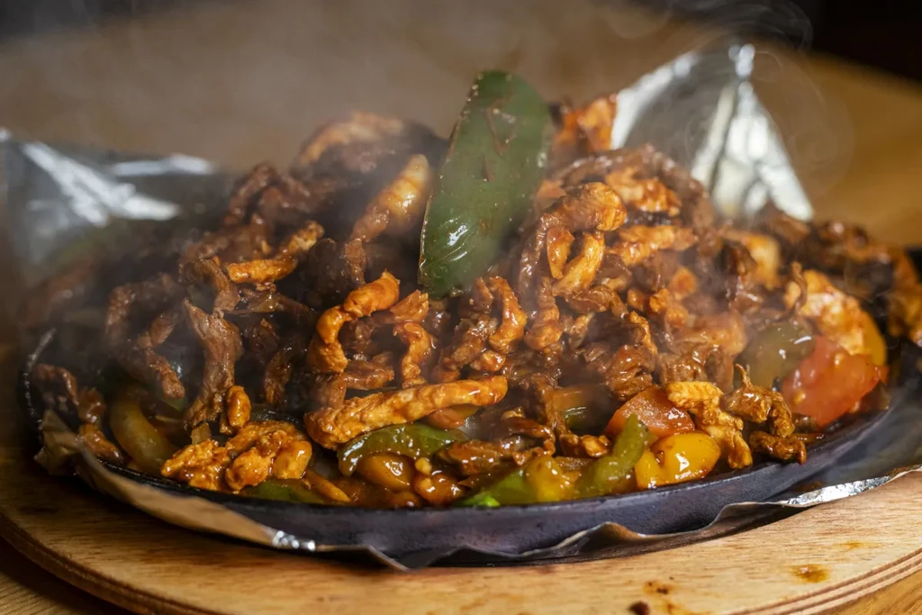 Sizzling beef and chicken fajitas with peppers on a cast-iron skillet.