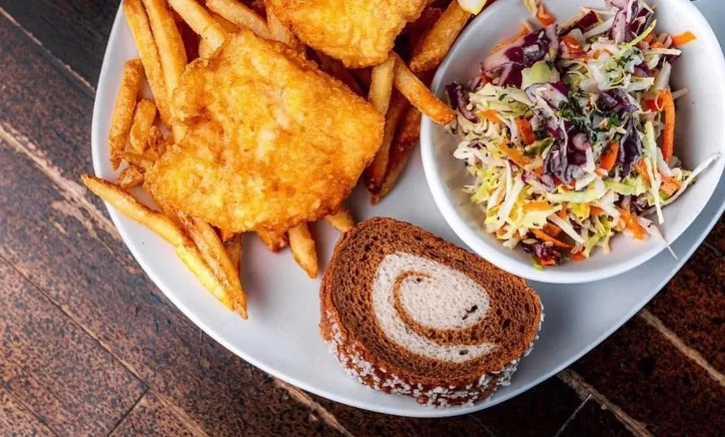 Plate of fish and chips, coleslaw, and marble rye bread.