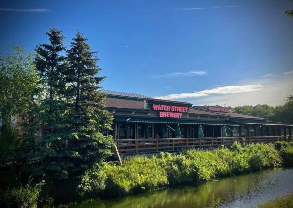 Water Street Brewery building and covered patio by a sunny river.