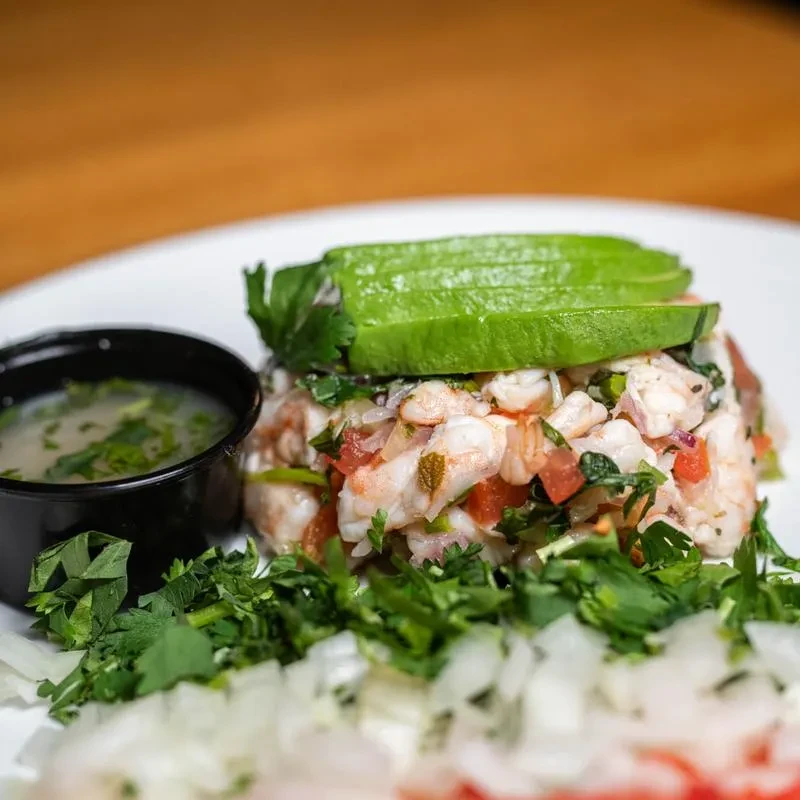 Top-down shrimp ceviche with avocado, tomatoes, onions, herbs, and sauce.