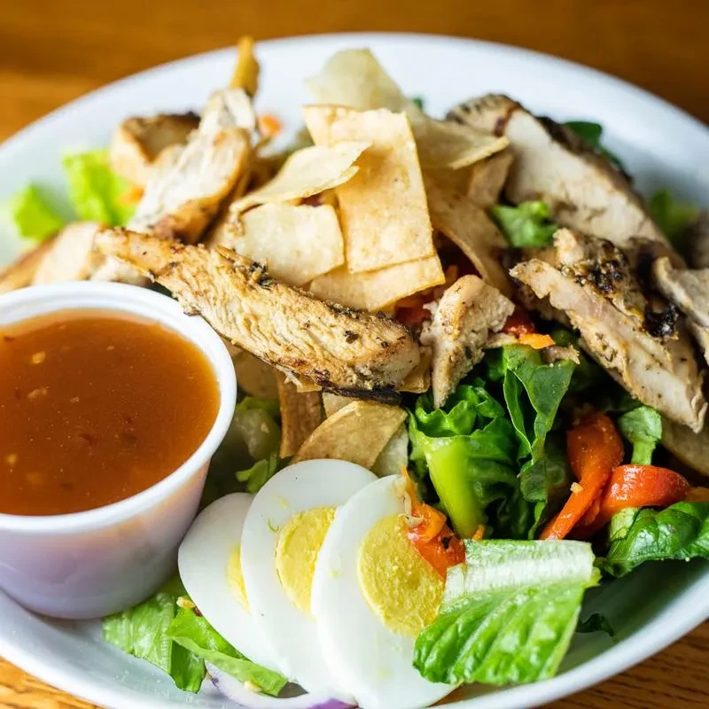 Overhead, vibrant grilled chicken salad with egg and tortilla strips.