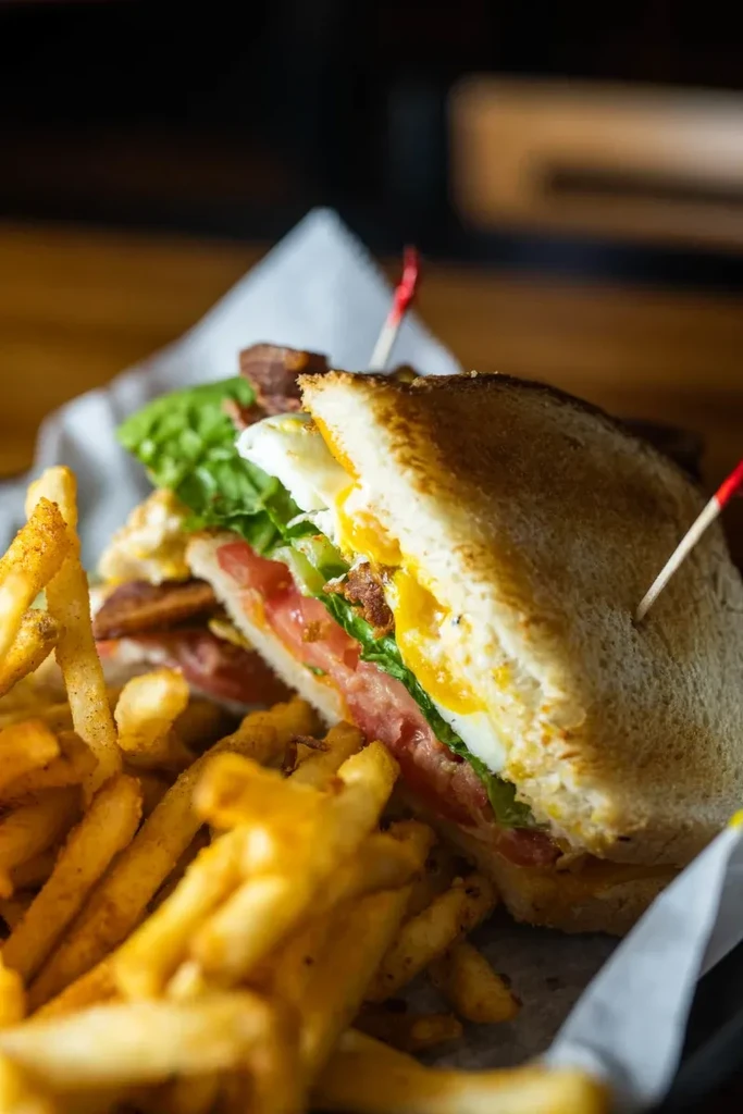 Club sandwich with fried egg, bacon, lettuce, and golden french fries.