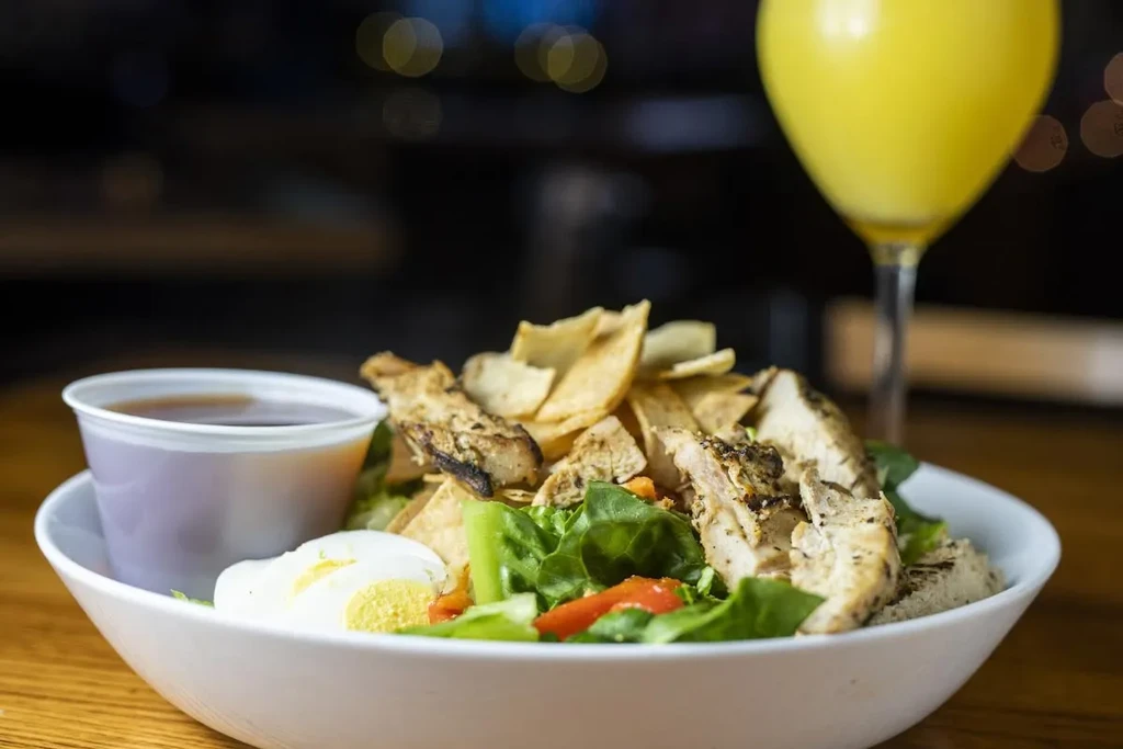 White bowl of grilled chicken salad with egg and dressing.