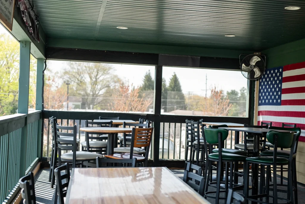 Empty restaurant patio with tables, chairs, an American flag, and outside view.