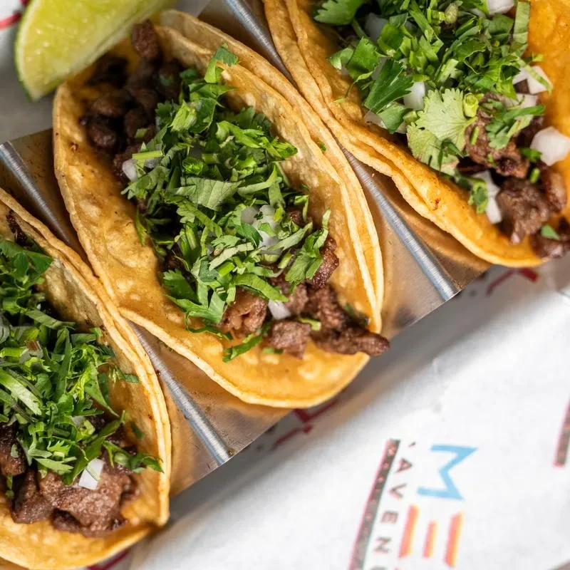 Three street tacos in a holder with meat, cilantro, onion, lime.