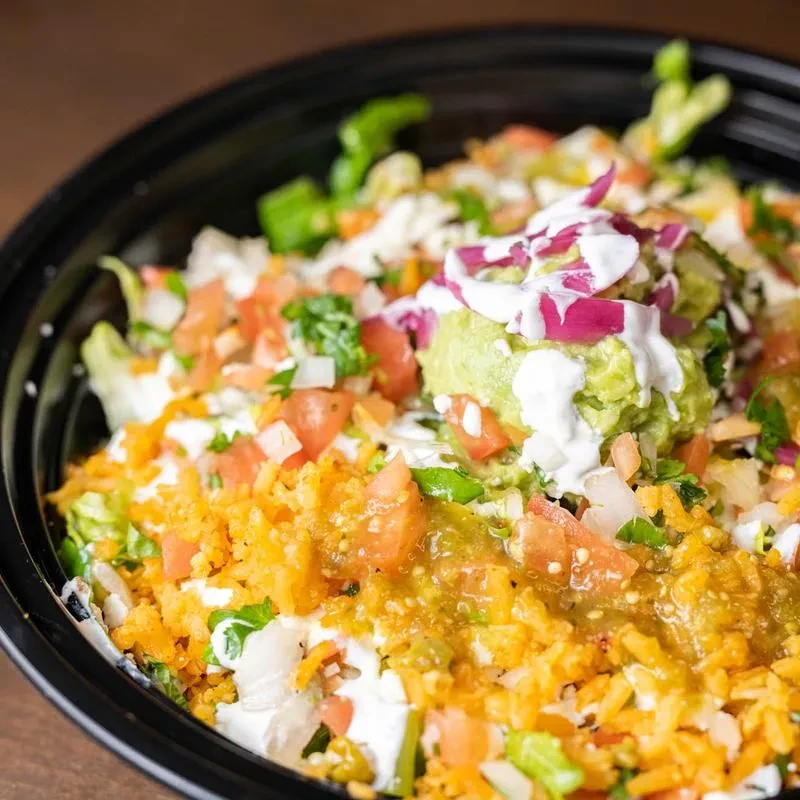 Colorful rice bowl with orange rice, lettuce, tomatoes, guacamole, and sour cream.