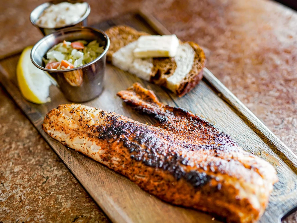 Grilled fish meal with sides on a wooden board.