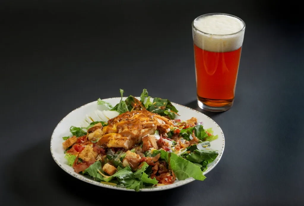 Well-lit studio shot of a chicken salad and a pint of beer.