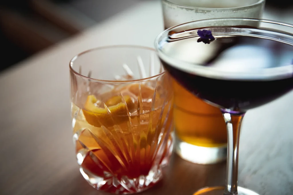 Close-up of three cocktails, two in focus, with flower and citrus peels.