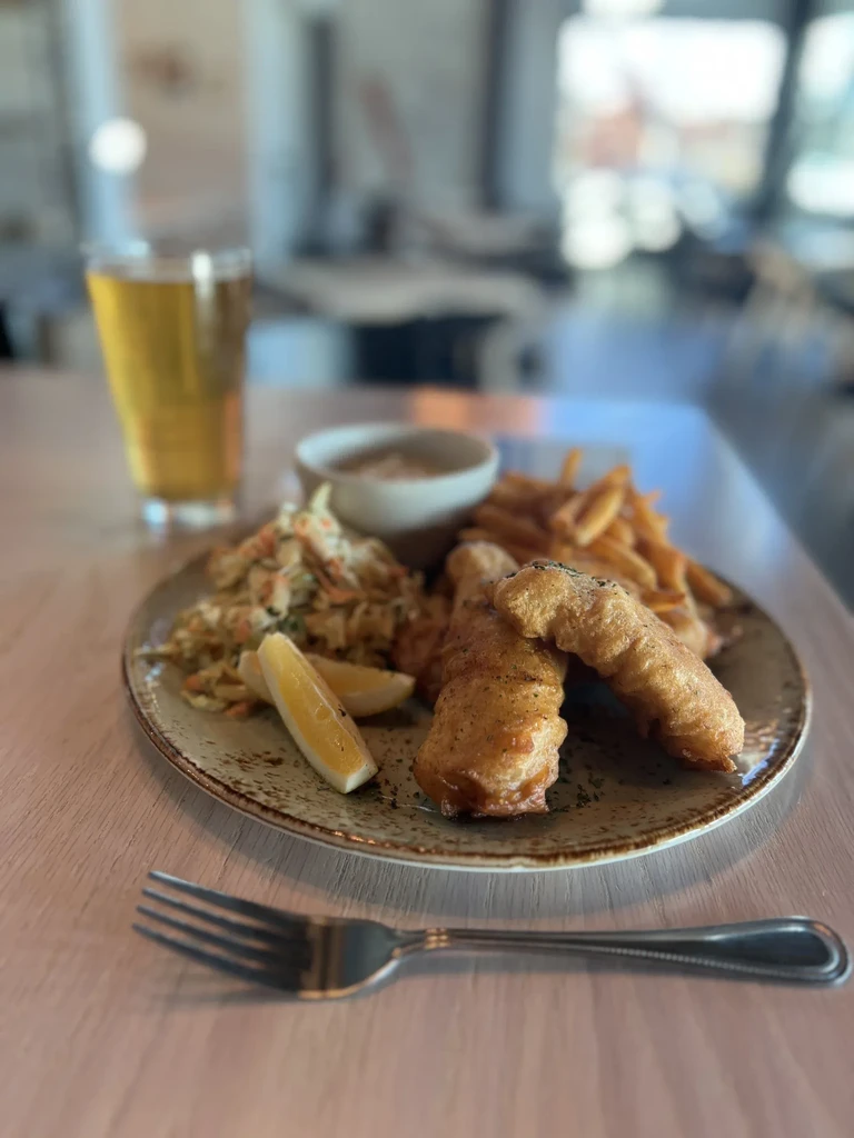 Plate of fish and chips, coleslaw, lemon, dipping sauce, and beer.