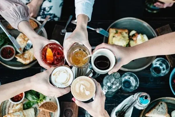 High-angle view of hands clinking drinks and brunch dishes.