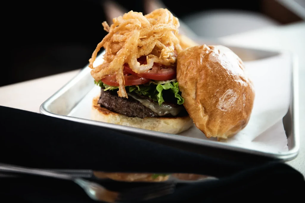 Gourmet burger with melted cheese, lettuce, tomatoes, and crispy onion strings.