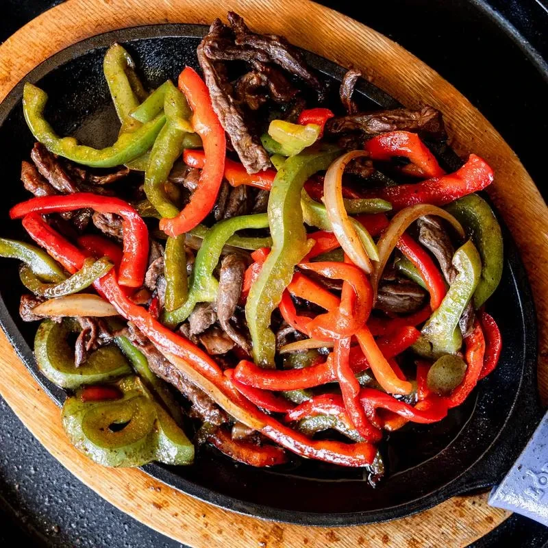 Sizzling beef fajitas with colorful bell peppers and onions in a skillet.
