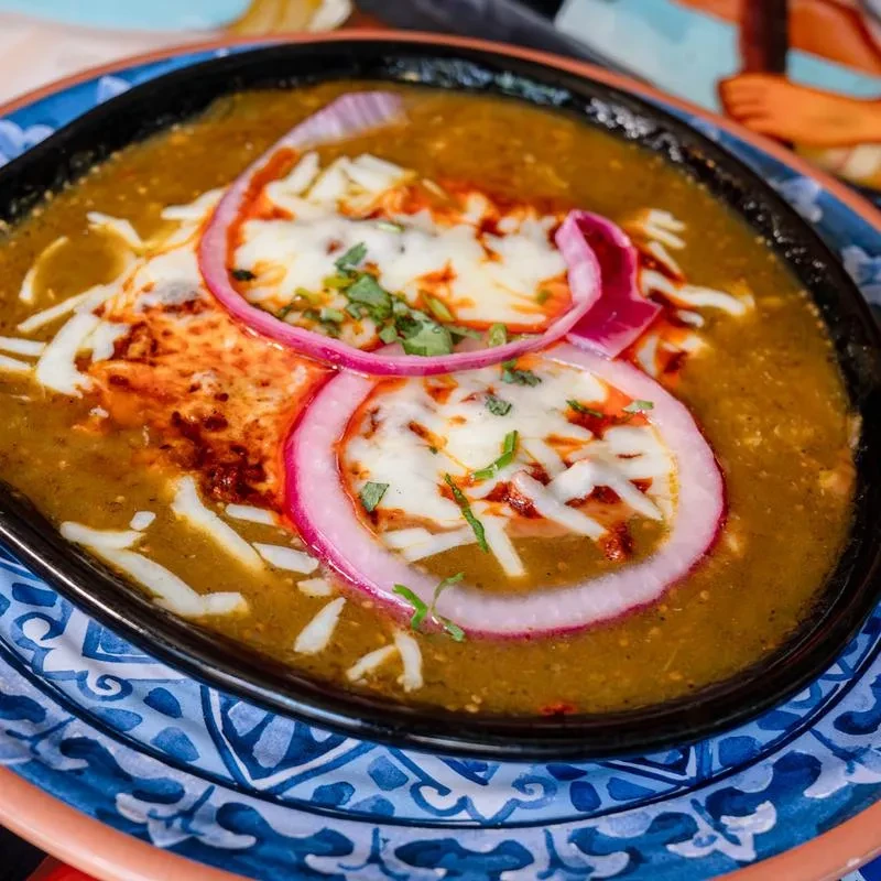 Greenish-brown stew topped with melted cheese, red onion, and herbs.