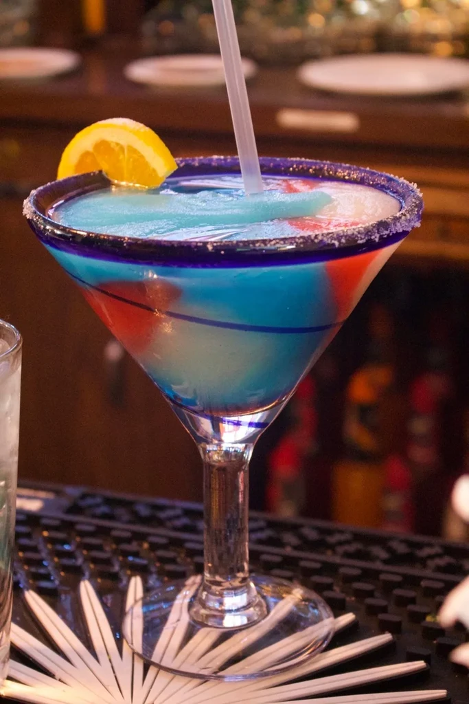 Layered blue, white, red frozen cocktail in martini glass, garnished.
