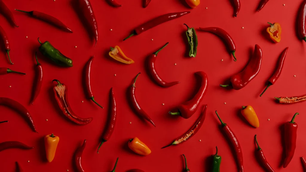 Flat lay of various red, green, yellow chili peppers on a red background.