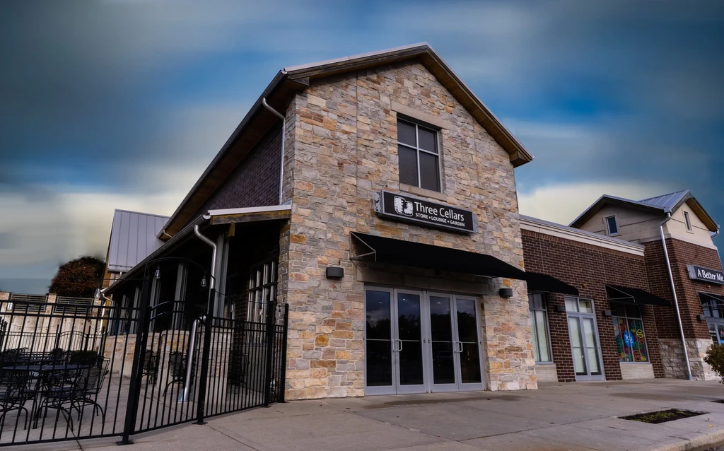 Modern stone building with gabled roof, 'Three Cellars' sign, and patio.