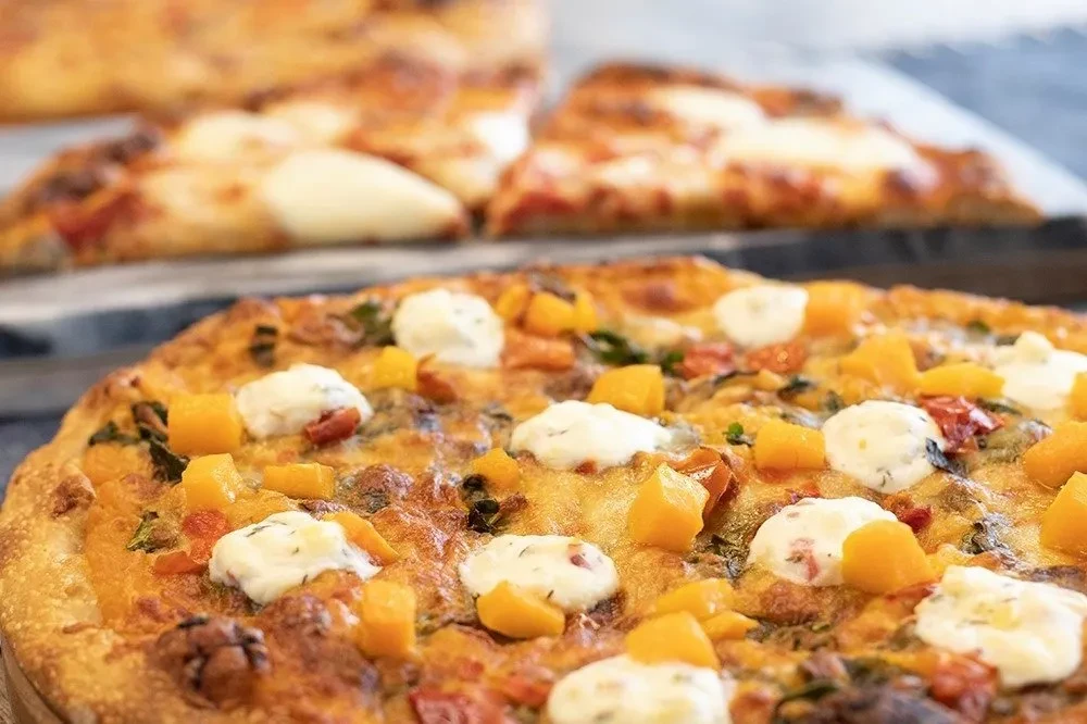 Rustic pizza topped with squash, creamy cheese, tomatoes, and herbs.