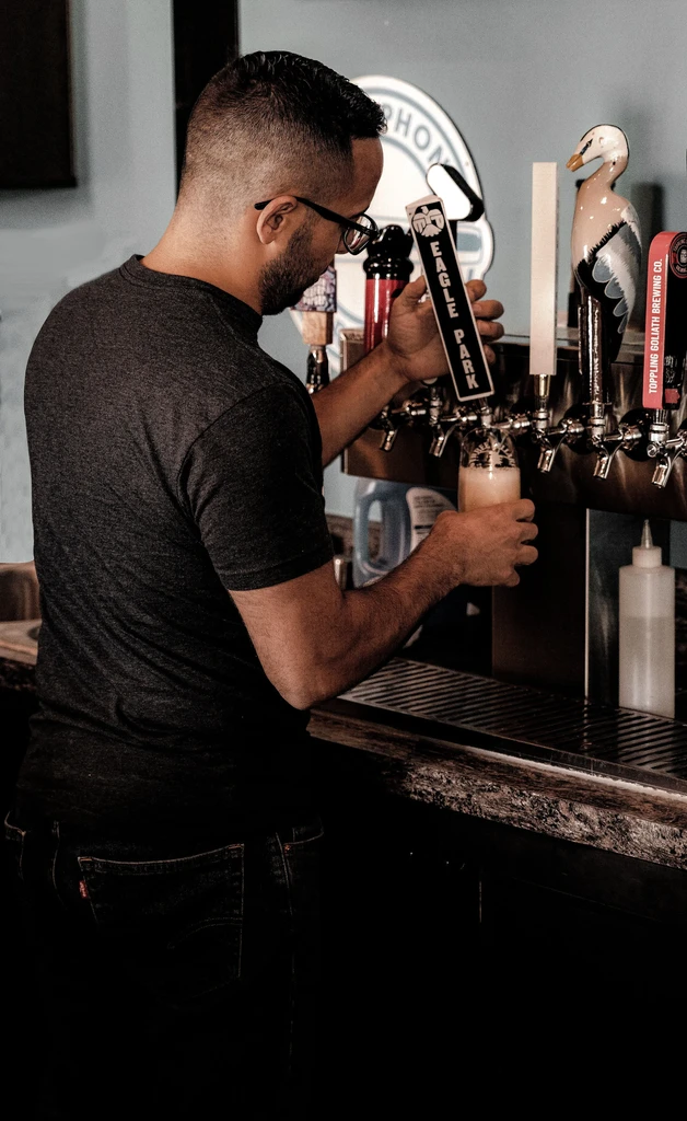 Bartender pouring a frothy beer from a tap.