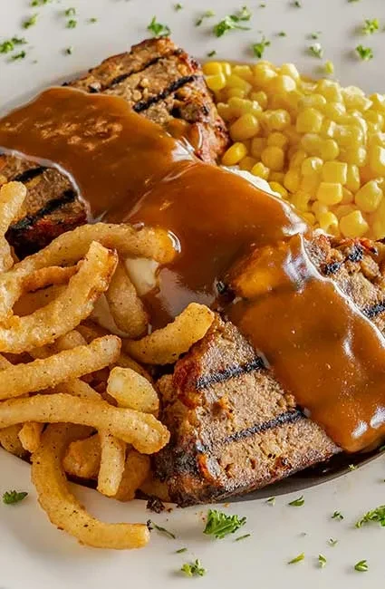 Meatloaf with gravy, mashed potatoes, corn, and curly fries.