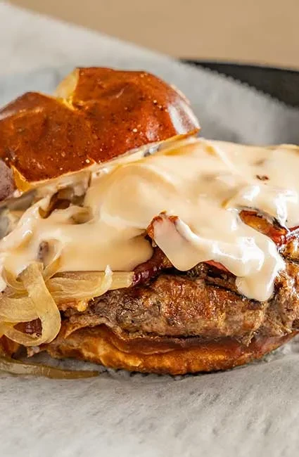 Substantial burger with pretzel bun, creamy sauce, onions, and bacon.