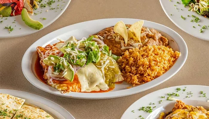 Overhead shot of two enchiladas with rice, beans, avocado, and cheese.