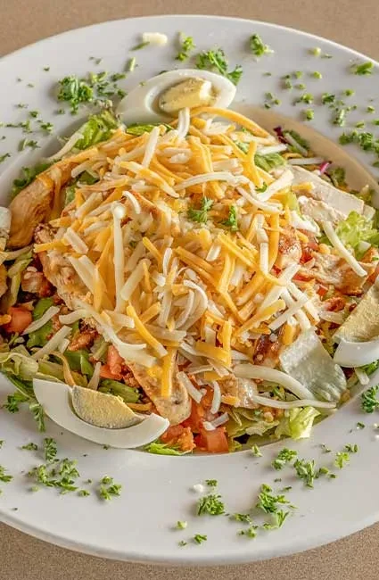 Overhead salad with chicken, shredded cheese, eggs, tomatoes, and lettuce.