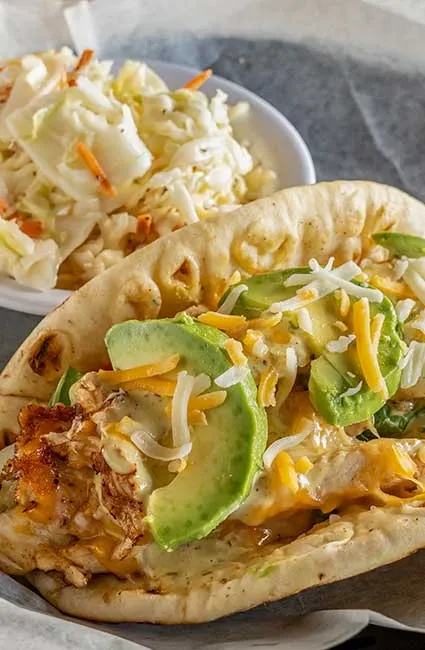 Pulled chicken flatbread with melted cheese, avocado, and side coleslaw.