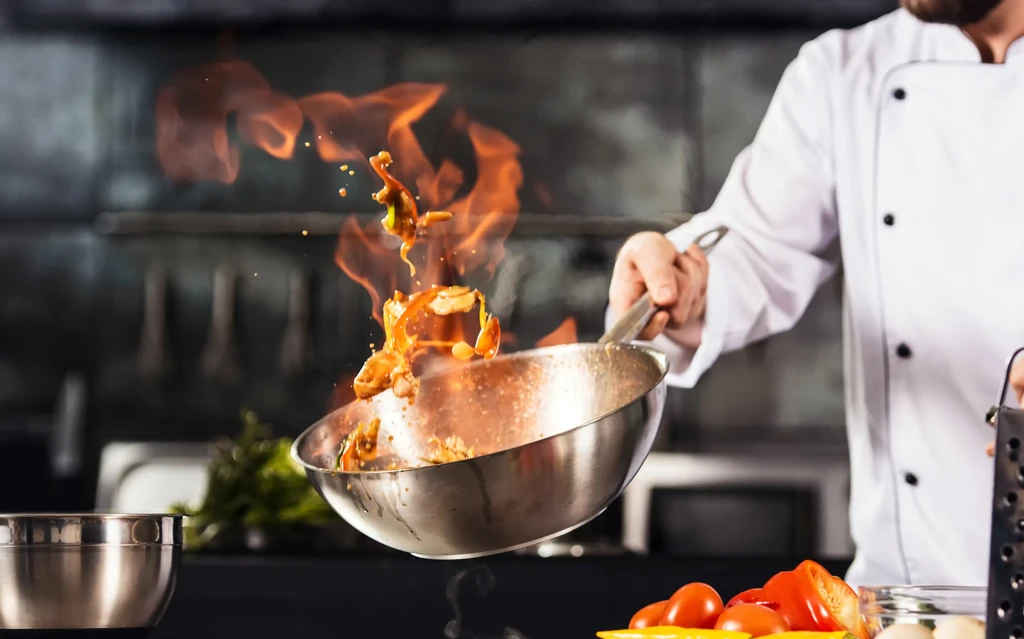 Chef tosses food in a flaming wok in a professional kitchen.