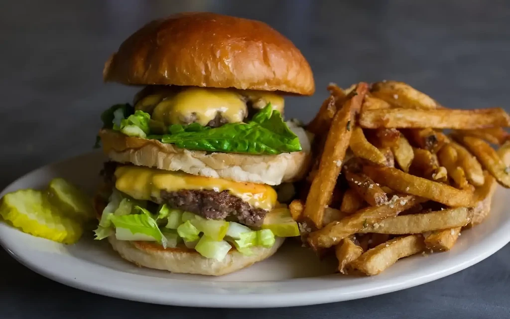 Double cheeseburger, crispy fries, and sliced pickles on a plate.