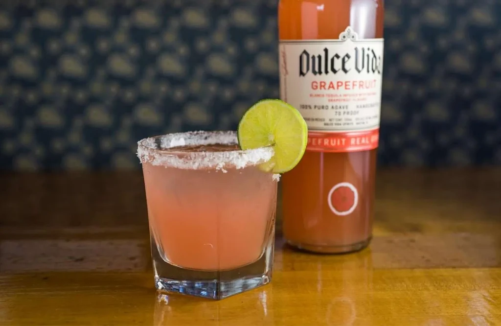 Grapefruit cocktail with salted rim and lime, featuring Dulce Vida bottle.