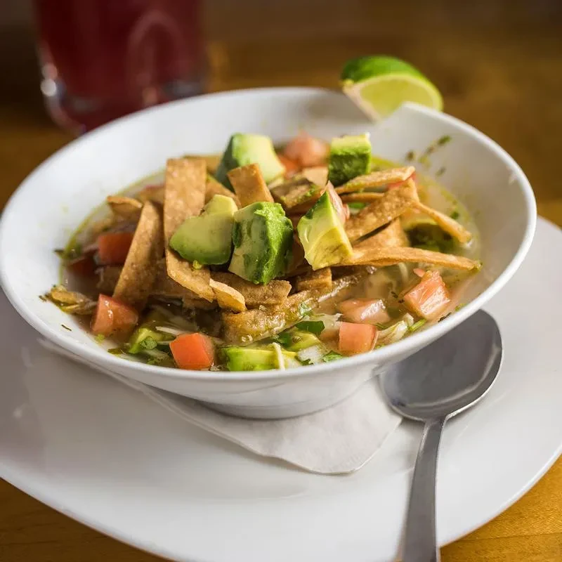 Bowl of tortilla soup with avocado, tomatoes, and lime wedge.