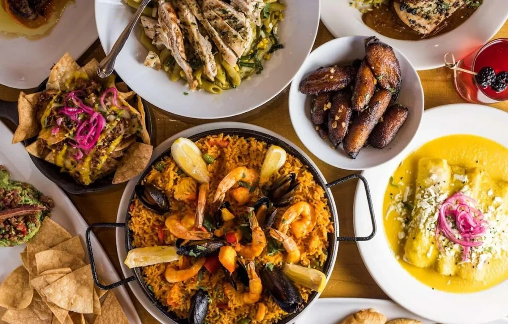 Diverse food spread: paella, nachos, enchiladas, plantains, and a drink.