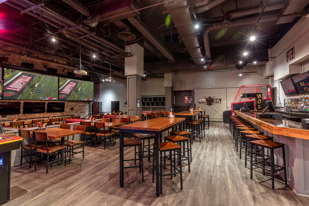 Empty modern sports bar with brick wall, multiple screens, and bar.