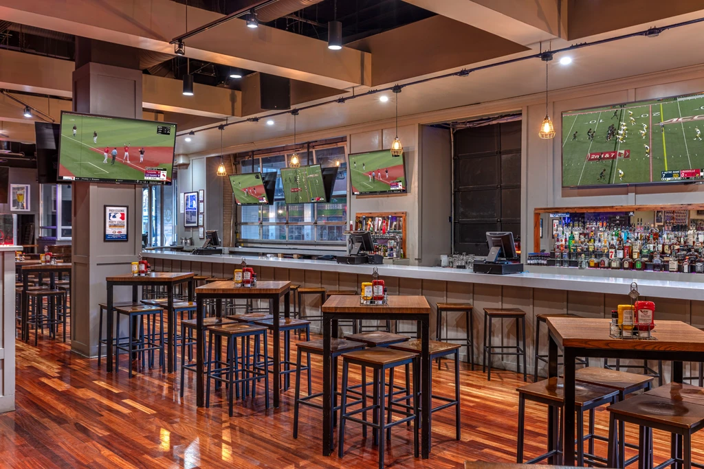 Modern sports bar interior with high-top tables, bar, and sports on TVs.