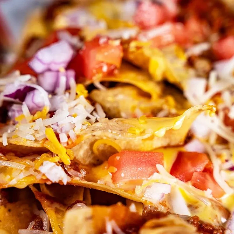 Close-up: nachos with melted cheese, white sauce, tomatoes, onions, and meat.