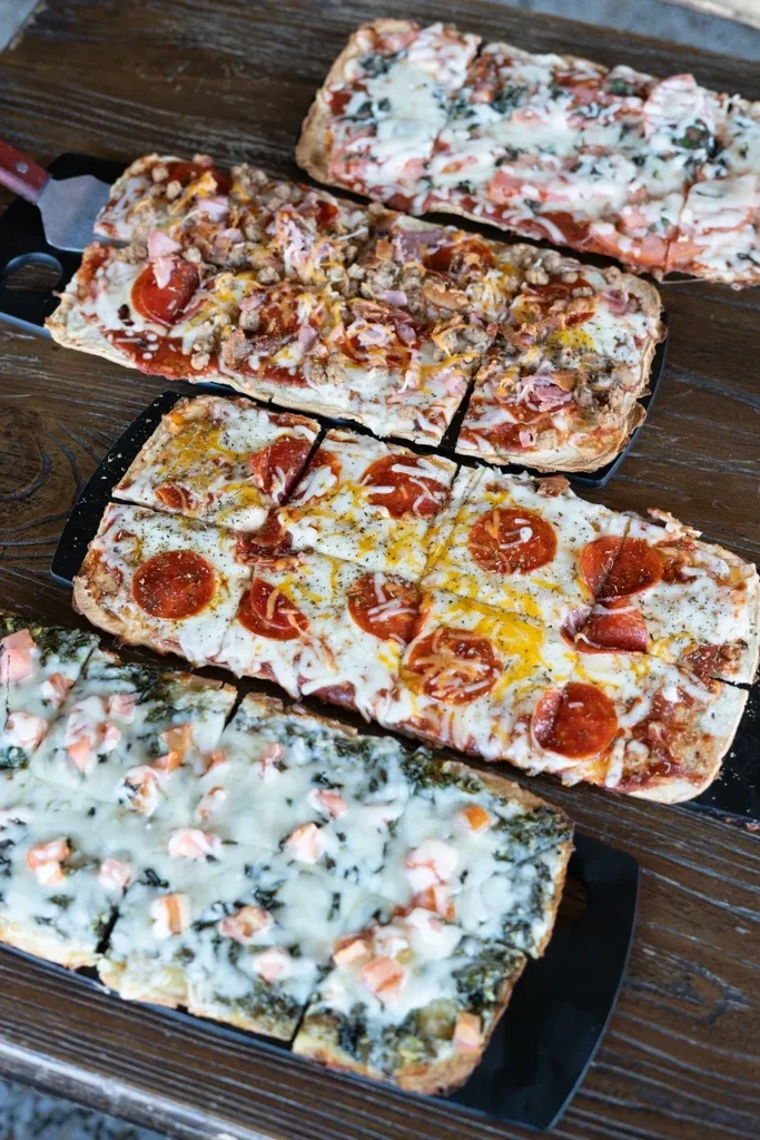 Four rectangular pizzas with different toppings on a wooden table.