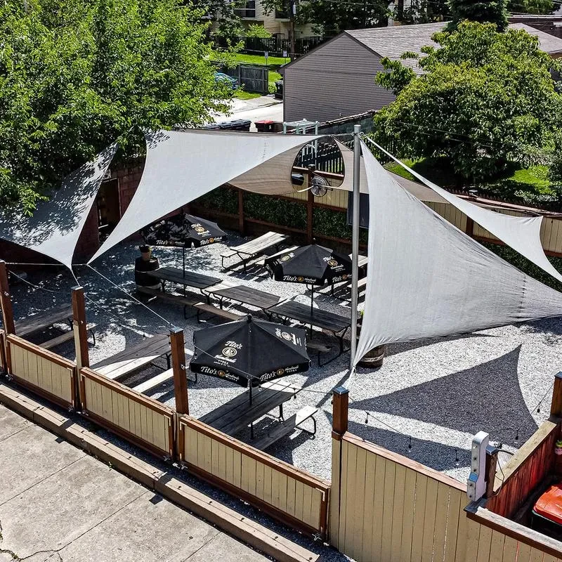 Outdoor patio with gravel, picnic tables, shade sails, and Tito's umbrellas.