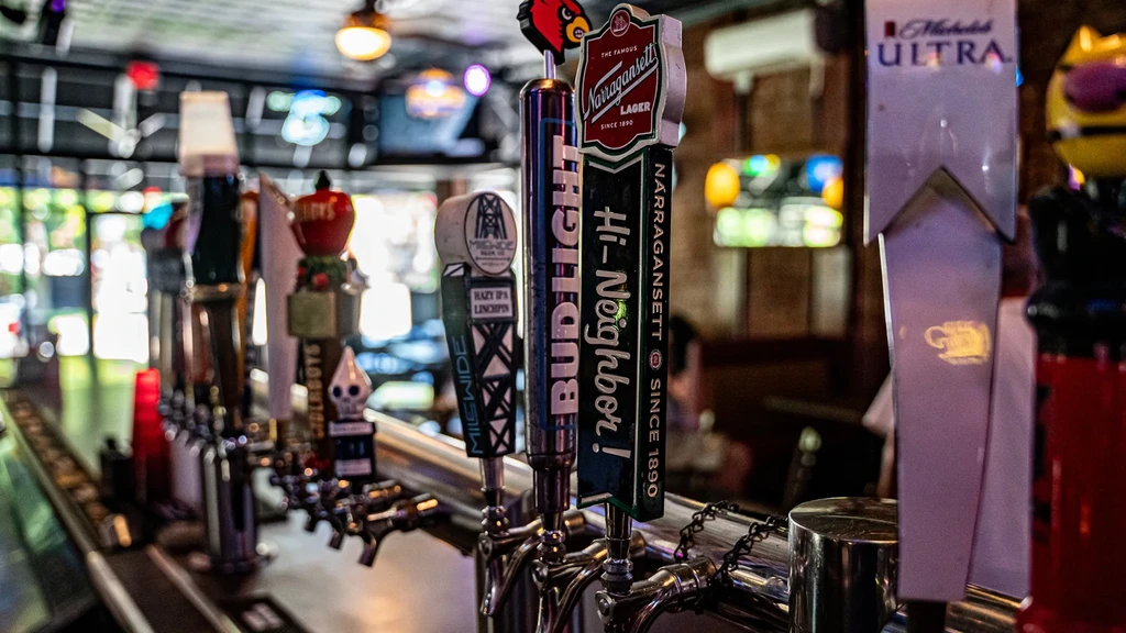 Row of diverse beer tap handles on a busy bar counter.